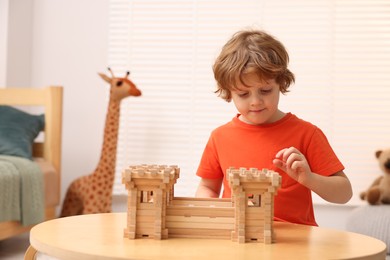 Photo of Cute little boy playing with wooden fortress at table in room. Child's toy