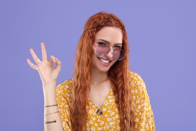 Photo of Stylish young hippie woman in sunglasses showing OK gesture on violet background