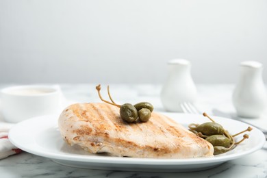 Photo of Delicious cooked chicken fillet with capers served on white marble table