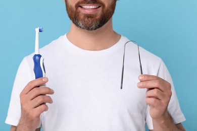 Photo of Man with tongue cleaner and plastic toothbrush on light blue background, closeup