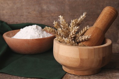 Photo of Mortar with spikes and bowl of wheat flour on wooden table, space for text