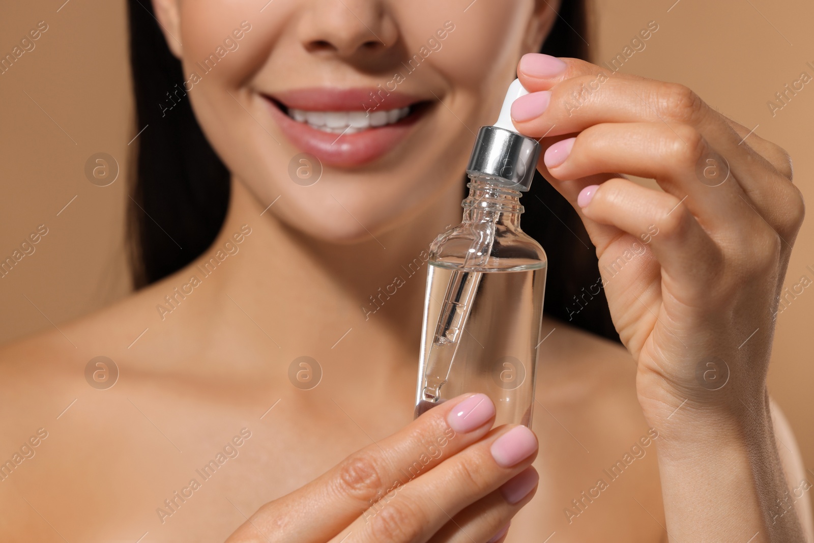 Photo of Young woman with serum in her hands on beige background, closeup