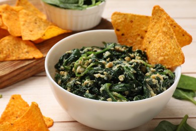 Photo of Tasty spinach dip with eggs in bowl and nachos chips on light wooden table, closeup