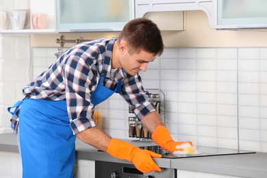 Man cleaning kitchen stove with sponge in house