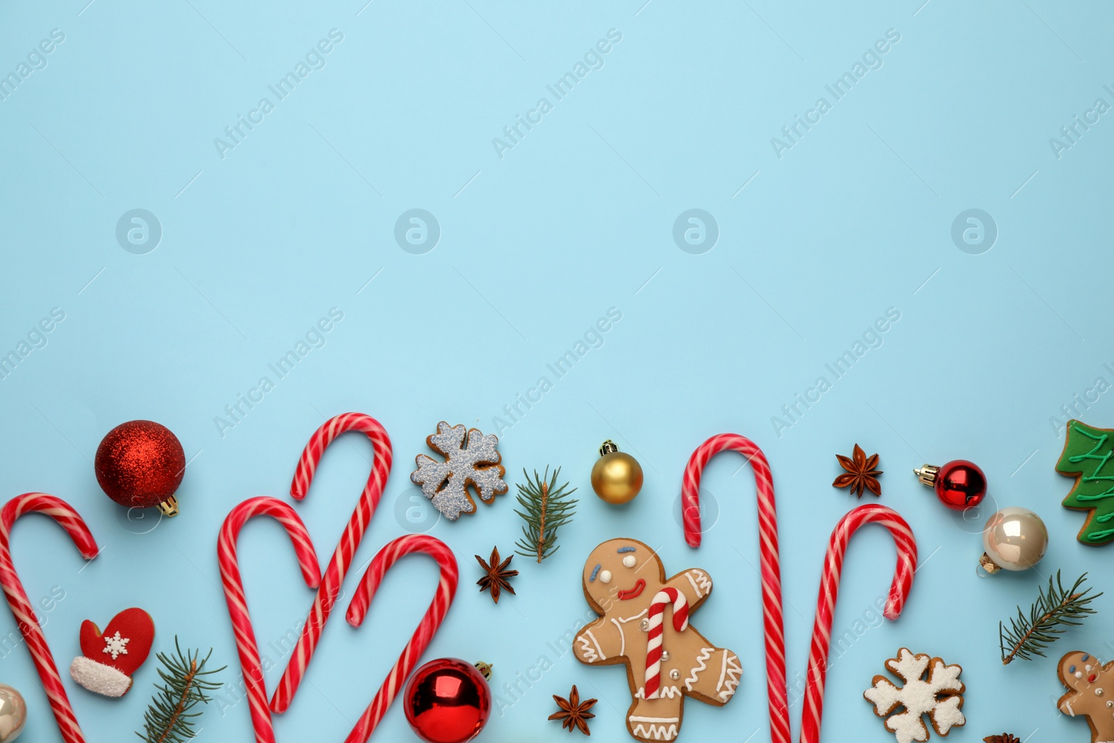 Photo of Flat lay composition with sweet candy canes and Christmas decor on light blue background, space for text