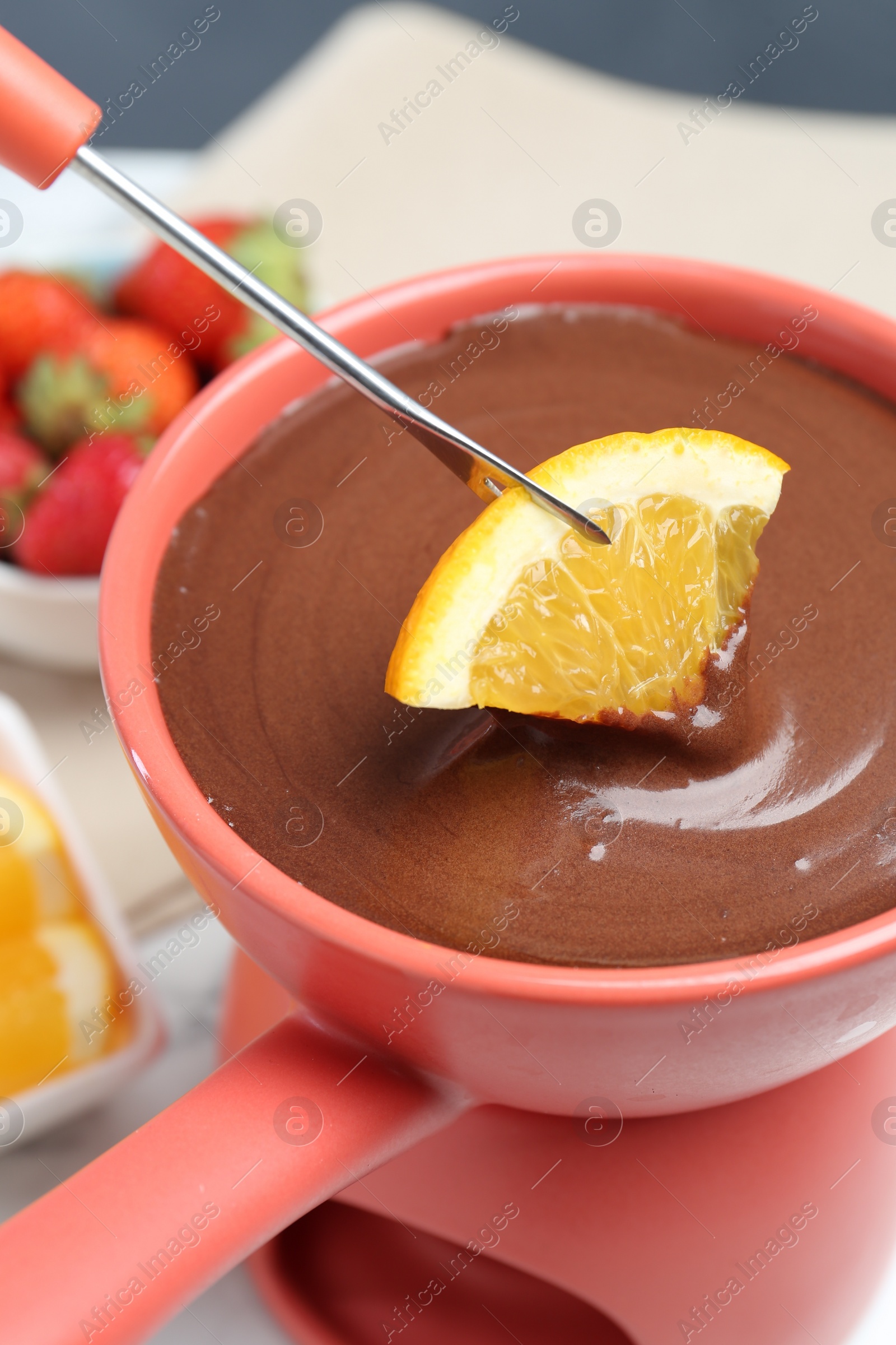 Photo of Dipping fresh orange into fondue pot with melted chocolate at table, closeup