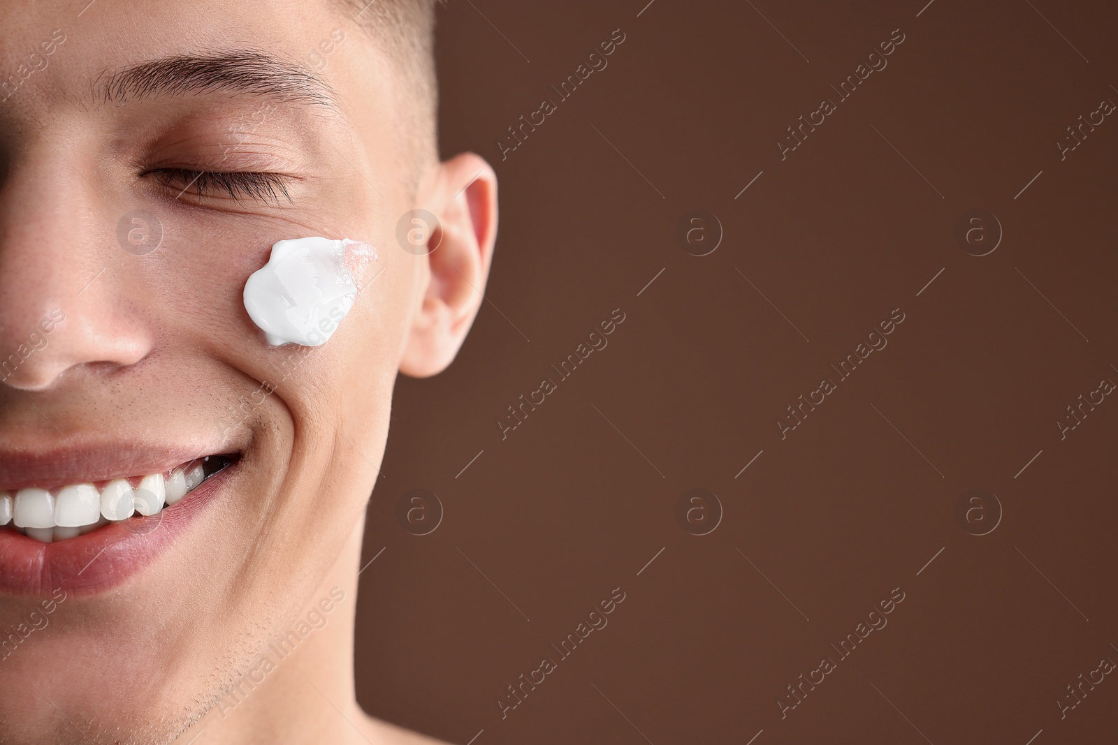 Photo of Handsome man with moisturizing cream on his face against brown background, closeup. Space for text