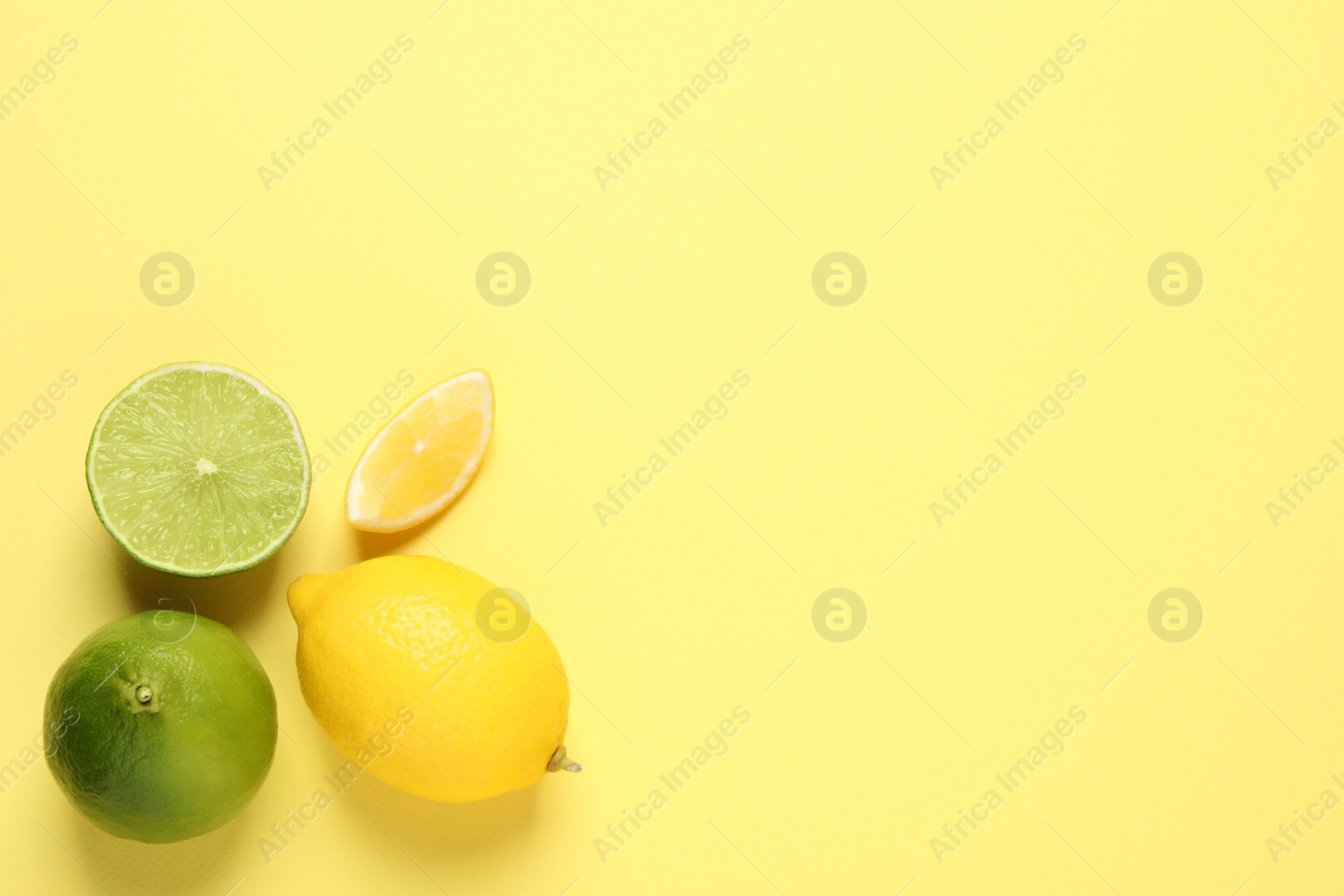 Photo of Fresh ripe lemons and limes on yellow background, flat lay. Space for text