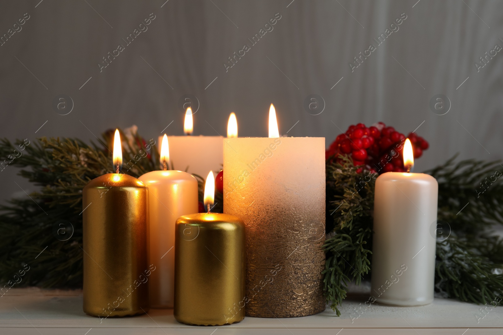 Photo of Different burning candles and Christmas decor on white wooden table