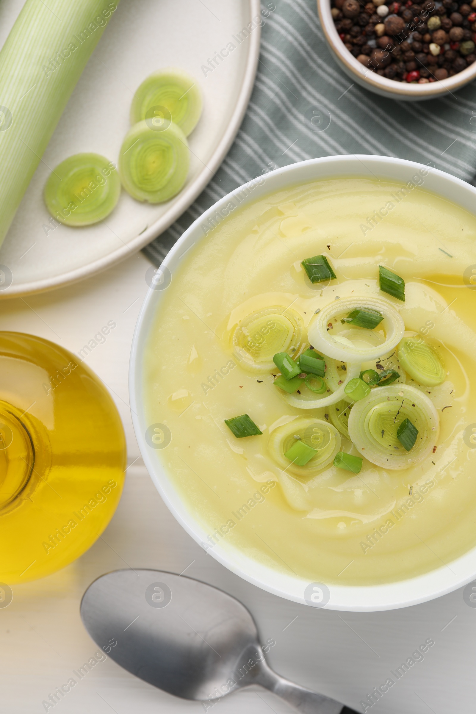 Photo of Bowl of tasty cream soup with leek and spoon on white wooden table, flat lay