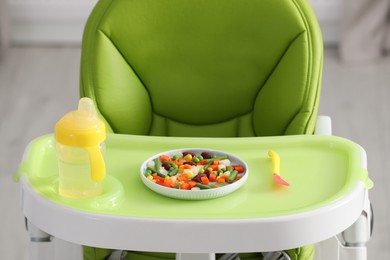 Photo of Baby high chair with healthy food and water indoors