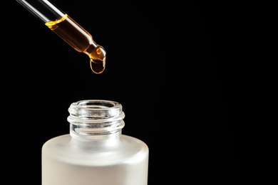 Photo of Pipette with oil over bottle on black background. Space for text