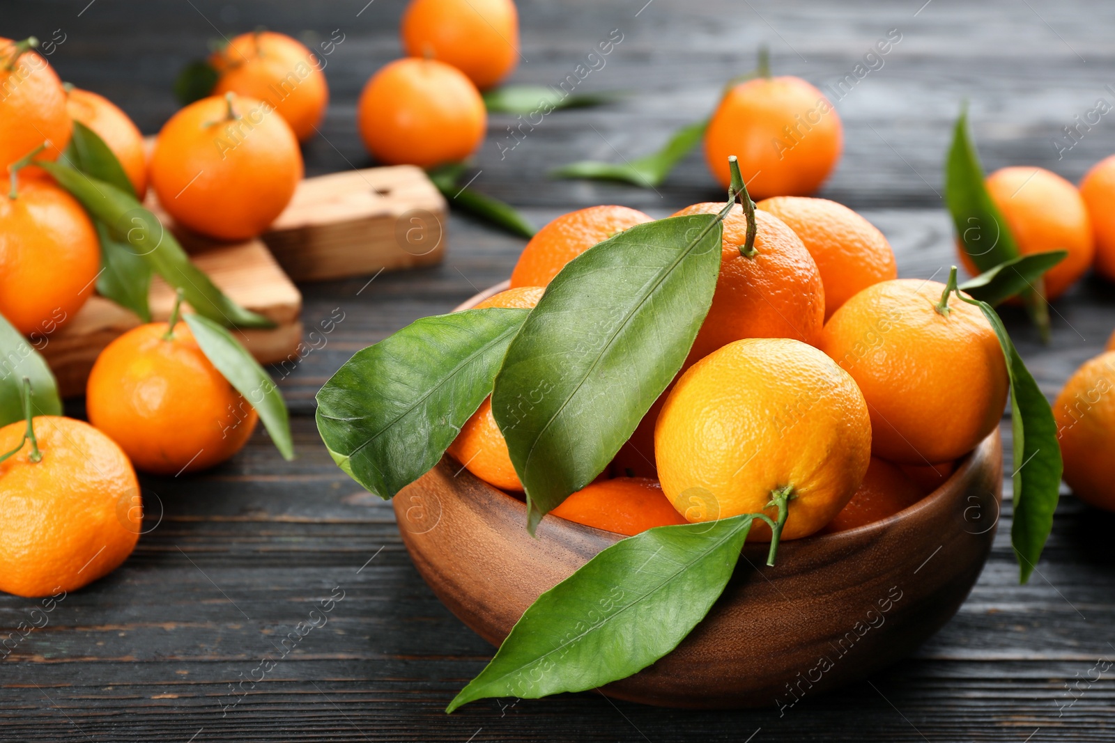 Photo of Fresh ripe tangerines with green leaves on black wooden table, closeup