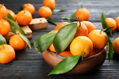 Photo of Fresh ripe tangerines with green leaves on black wooden table, closeup