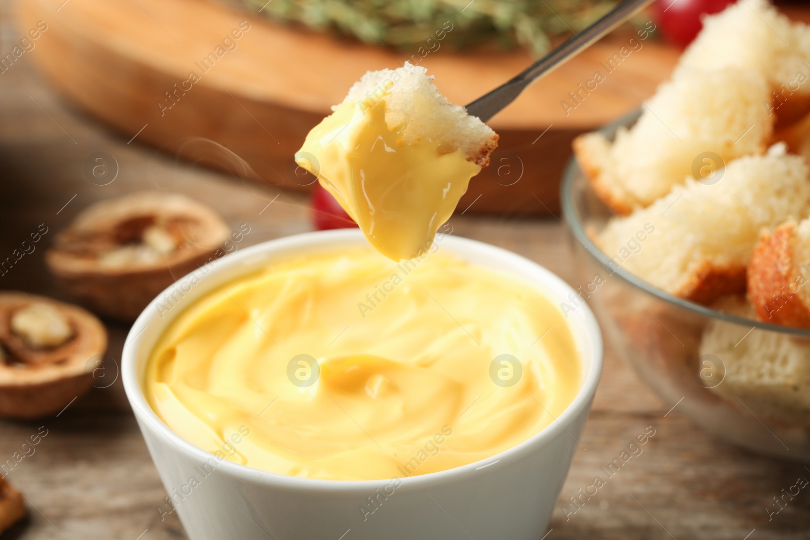 Photo of Piece of bread over bowl with delicious cheese fondue on wooden table