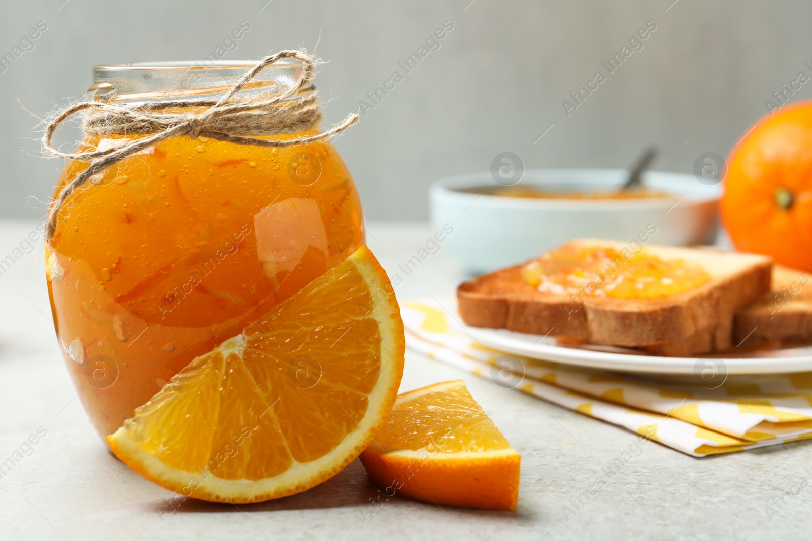 Photo of Delicious orange marmalade in glass jar on light grey table. Space for text