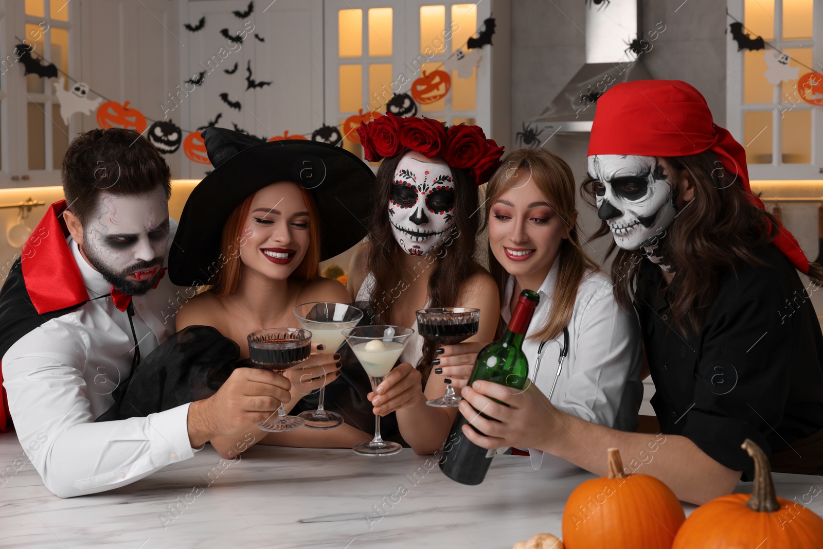 Photo of Group of people in scary costumes with cocktails celebrating Halloween indoors