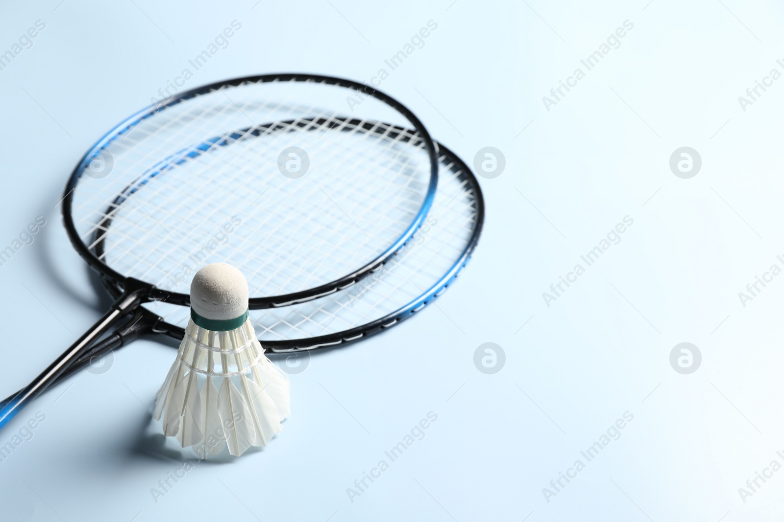 Photo of Feather badminton shuttlecock and rackets on light blue background, closeup. Space for text