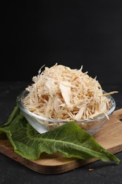 Photo of Grated horseradish in bowl, leaf and board on black table, closeup. Space for text