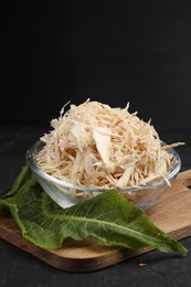 Grated horseradish in bowl, leaf and board on black table, closeup. Space for text