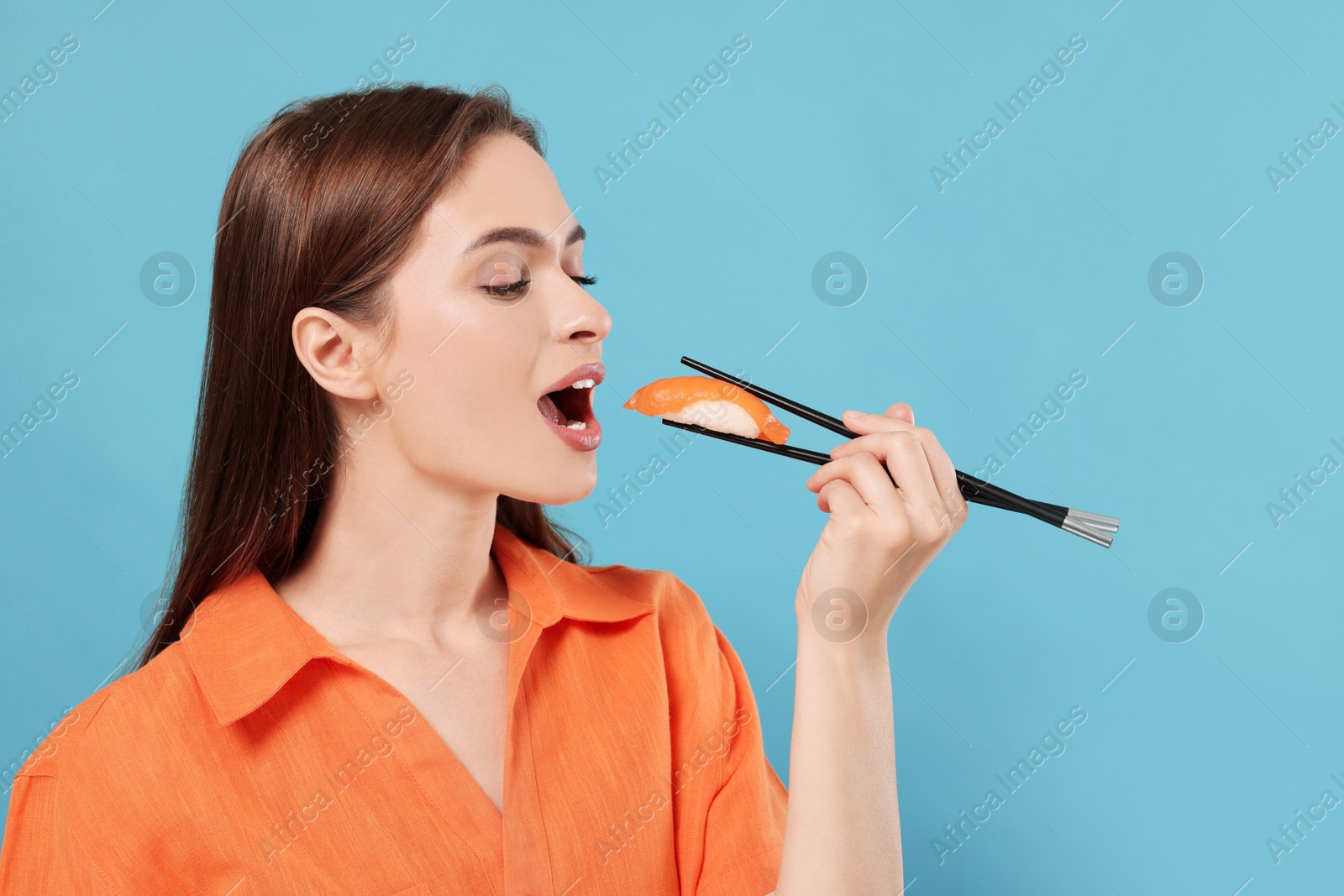 Photo of Beautiful young woman eating sushi with chopsticks on light blue background