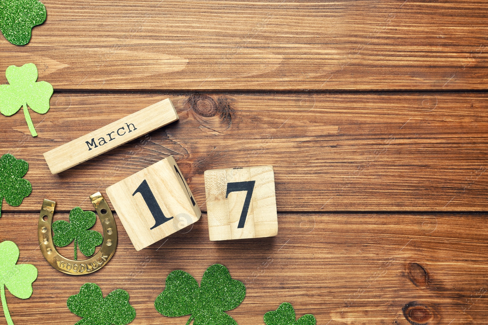 Photo of Decorative clover leaves, horseshoe and block calendar on wooden background, flat lay with space for text. St. Patrick's Day celebration