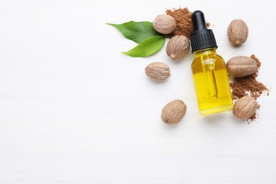 Bottle of nutmeg oil, nuts and powder on white wooden table, flat lay. Space for text