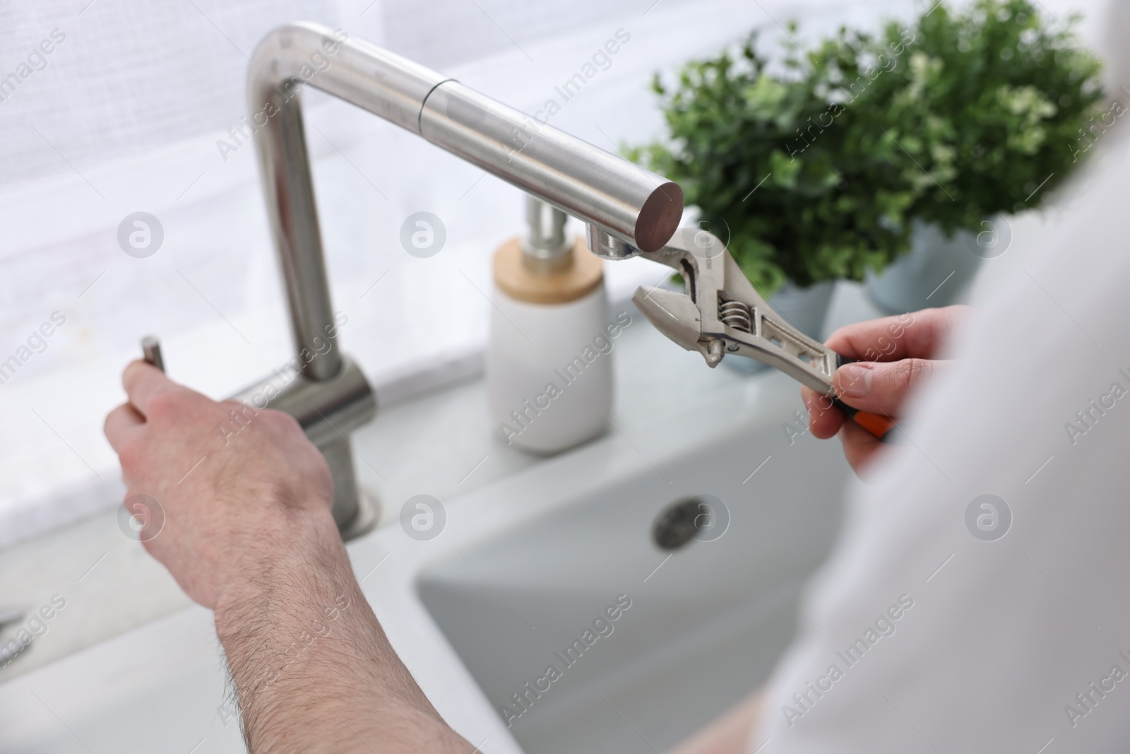 Photo of Plumber repairing faucet with spanner indoors, closeup