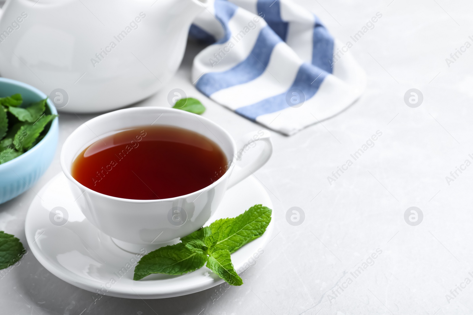 Photo of Cup with hot aromatic mint tea on light table, space for text