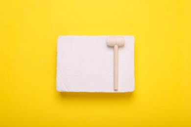 Educational toy for motor skills development. Excavation kit (plaster and wooden mallet) on yellow background, top view