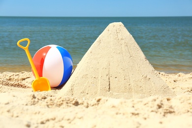 Photo of Sand pyramid, colorful ball and plastic shovel on beach near sea