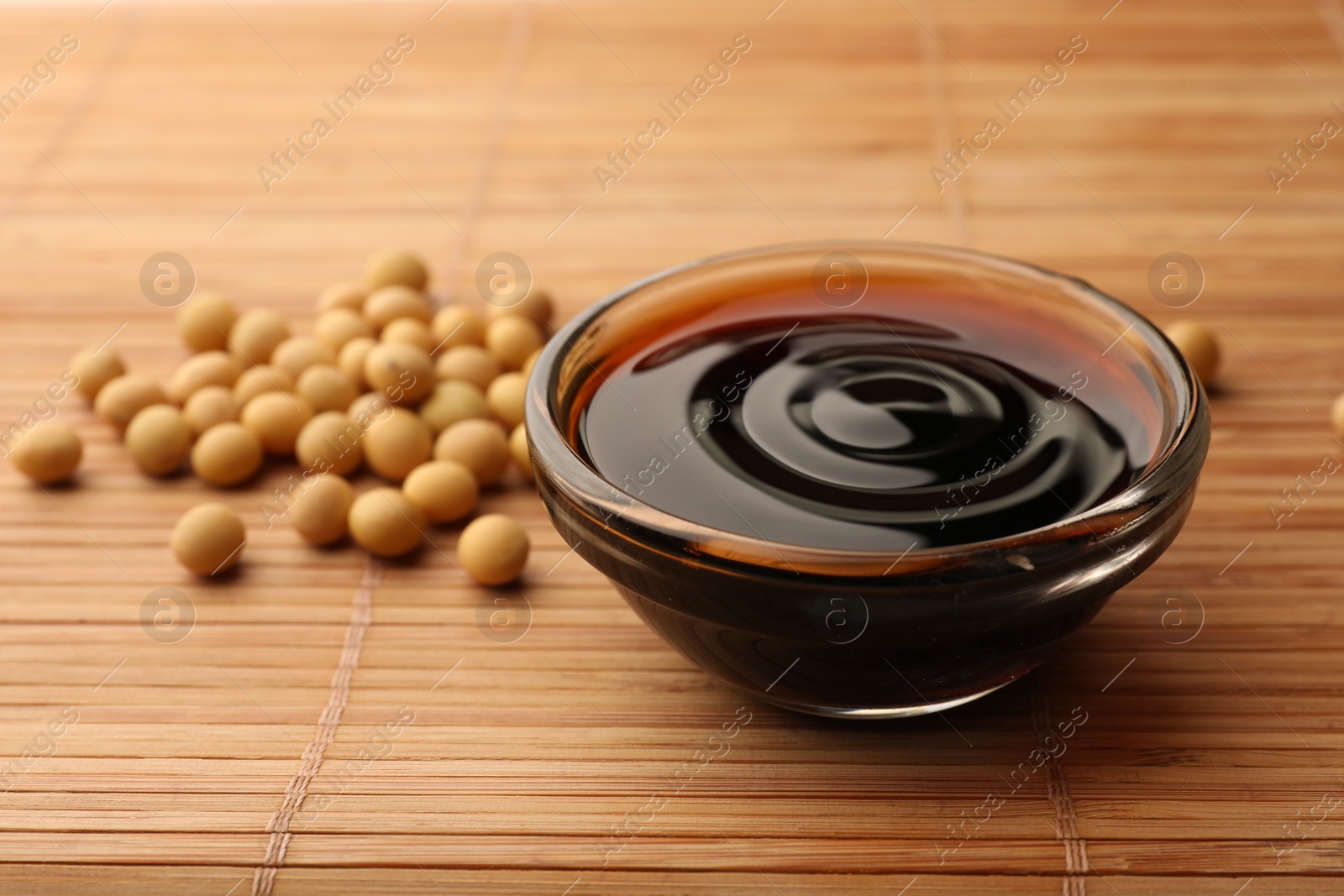 Photo of Soy sauce in bowl and soybeans on bamboo mat, closeup