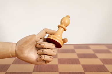 Photo of Robot with chess piece above board against light background, space for text. Wooden hand representing artificial intelligence