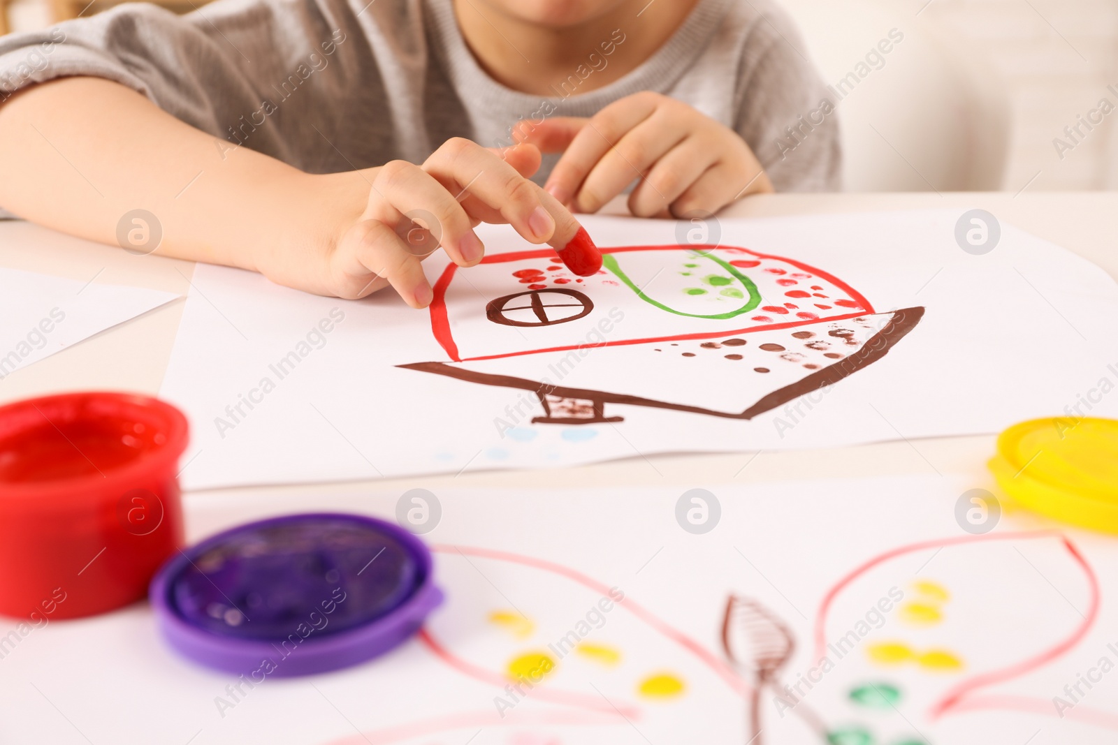 Photo of Little boy painting with finger at white table indoors, closeup