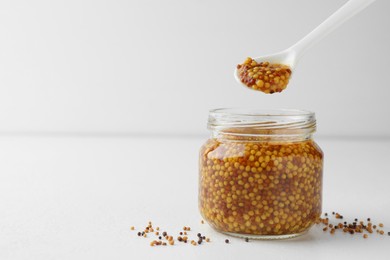 Taking whole grain mustard with spoon from jar on white table. Space for text