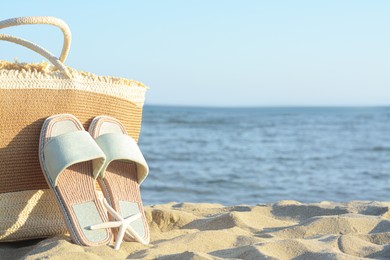 Photo of Straw bag, slippers and dry starfish on sandy beach near sea, space for text