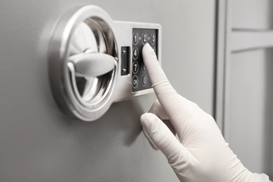 Woman in gloves entering code on keypad of modern safe, closeup