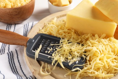 Grated, whole pieces of cheese and grater on table, closeup