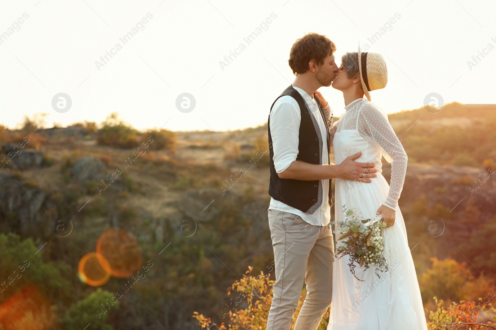 Photo of Happy newlyweds with beautiful field bouquet kissing outdoors