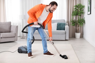 Photo of Young man cleaning carpet with vacuum at home