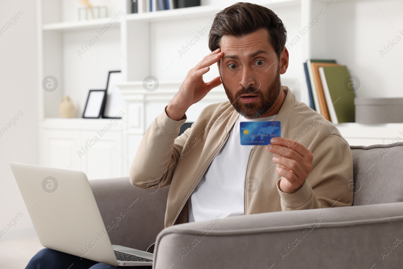 Photo of Shocked man with laptop and credit card in armchair at home. Be careful - fraud