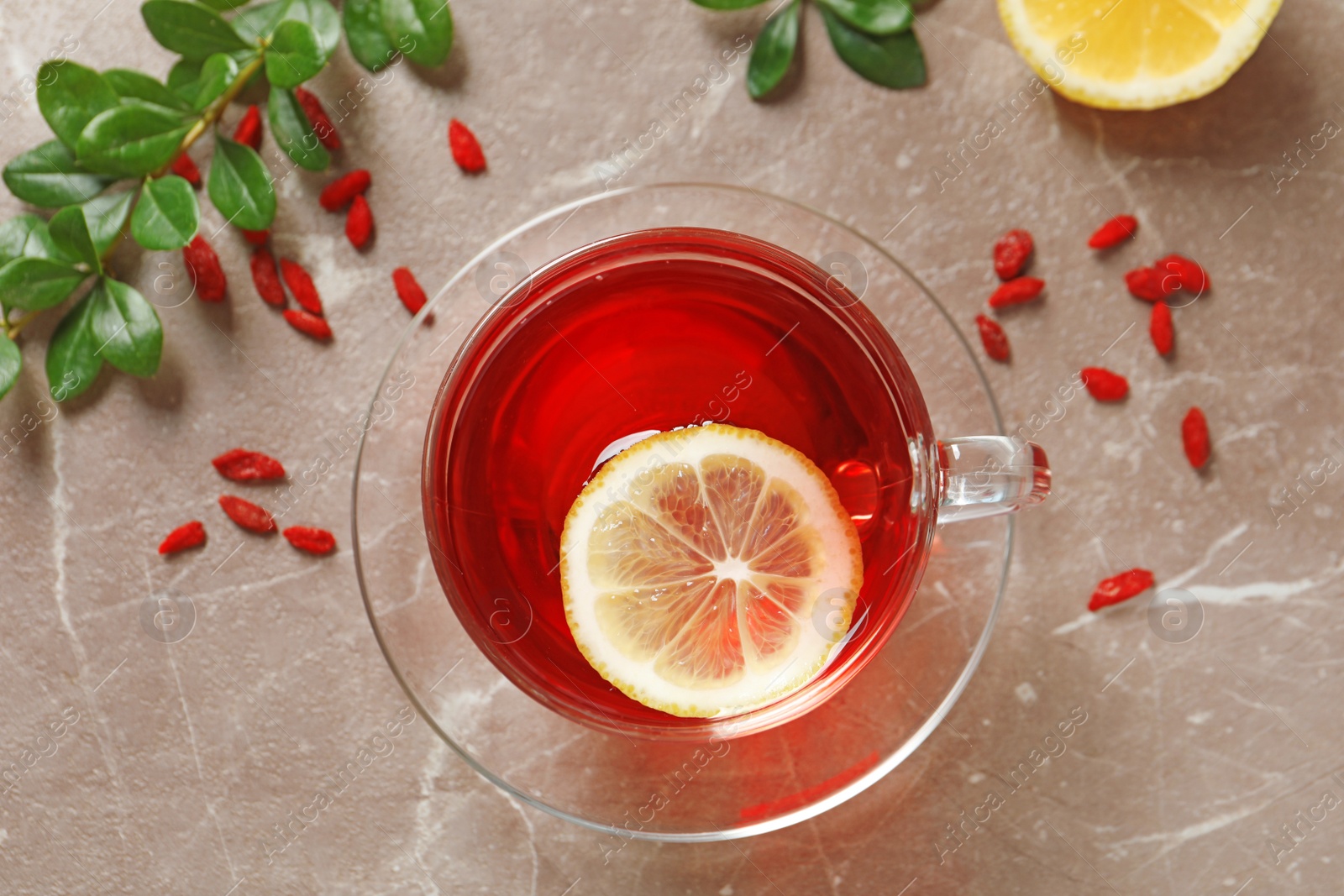 Photo of Glass cup of healthy goji tea with lemon on beige marble table, flat lay