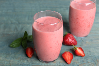 Photo of Tasty strawberry smoothies in glasses on blue wooden table