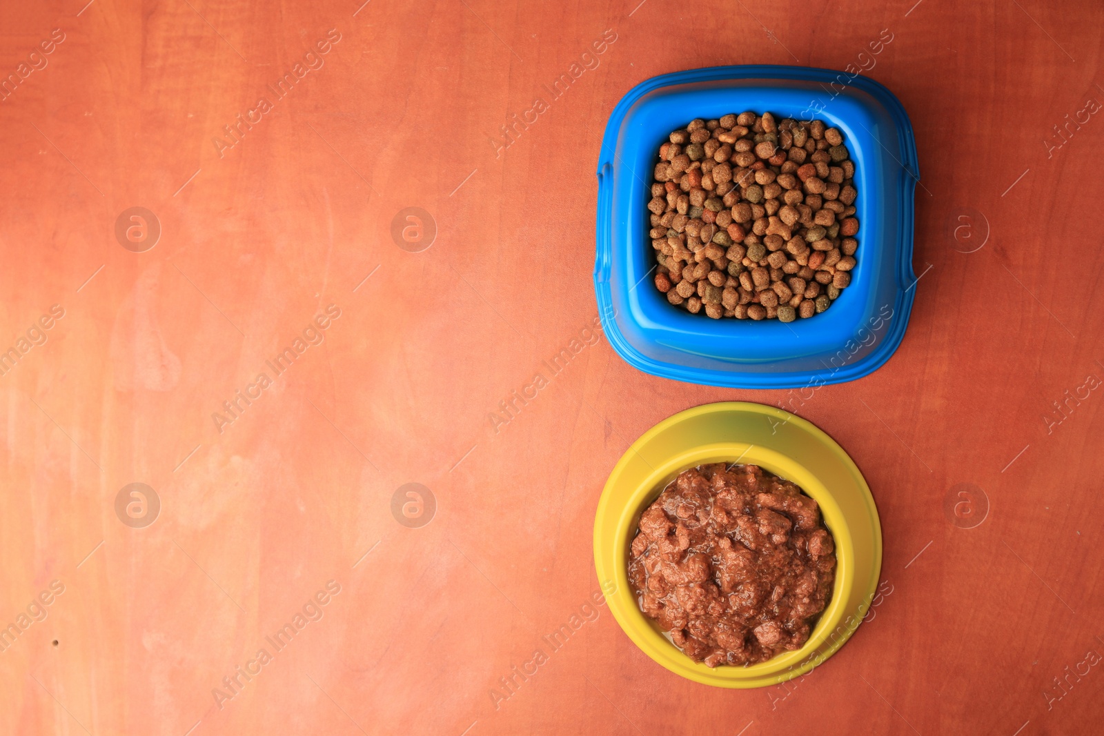 Photo of Dry and wet pet food in feeding bowls on orange background, flat lay. Space for text