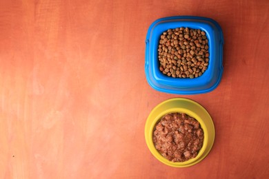 Photo of Dry and wet pet food in feeding bowls on orange background, flat lay. Space for text