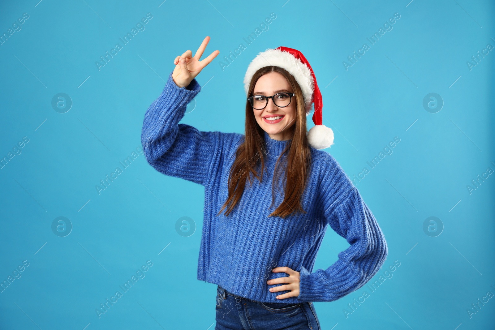 Photo of Young woman wearing Christmas sweater and Santa hat on blue background