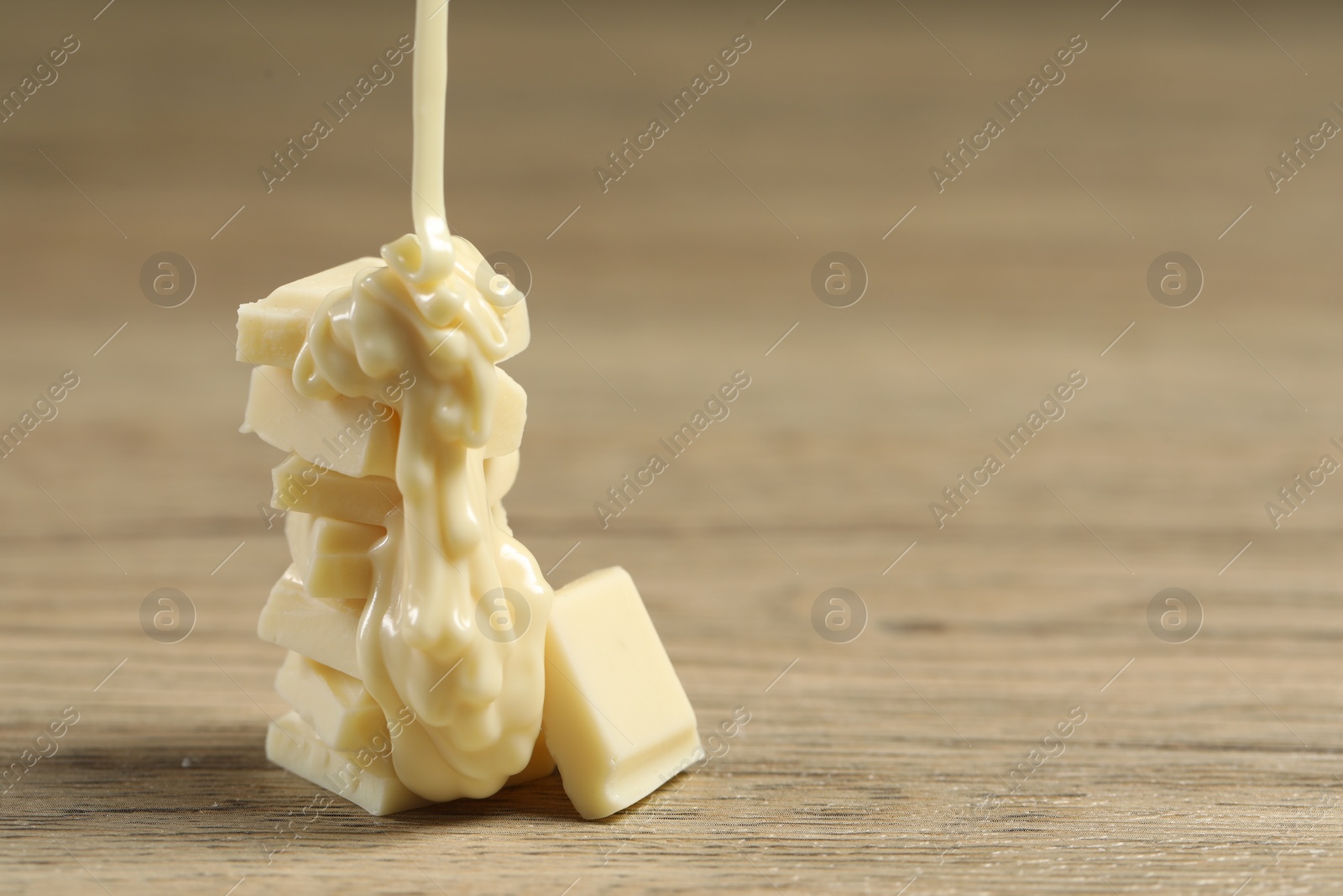 Photo of Pouring tasty white chocolate paste onto pieces on wooden table, closeup. Space for text