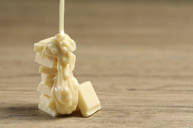 Photo of Pouring tasty white chocolate paste onto pieces on wooden table, closeup. Space for text
