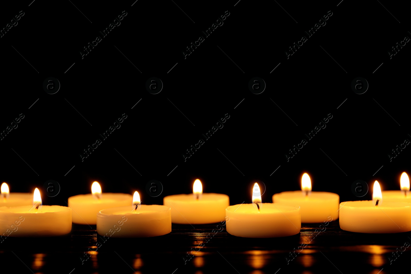 Photo of Burning candles on table against black background, space for text