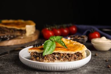 Piece of delicious pie with minced meat and basil served on grey table, closeup